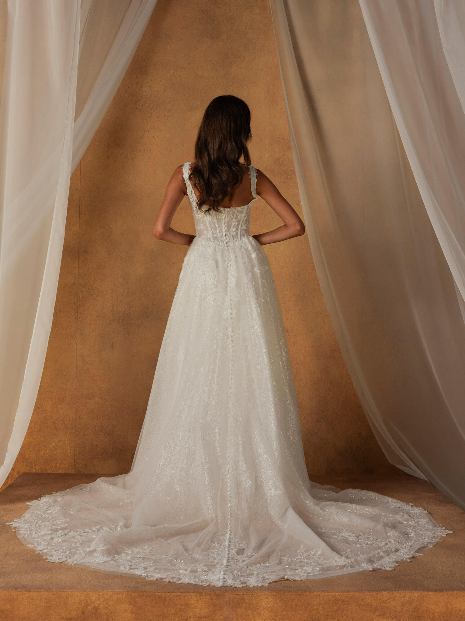 Rückenansicht eines Spitzen-Brautkleides mit langer und fließender Tüllschleppe, ideal für Hochzeiten in Bremen.