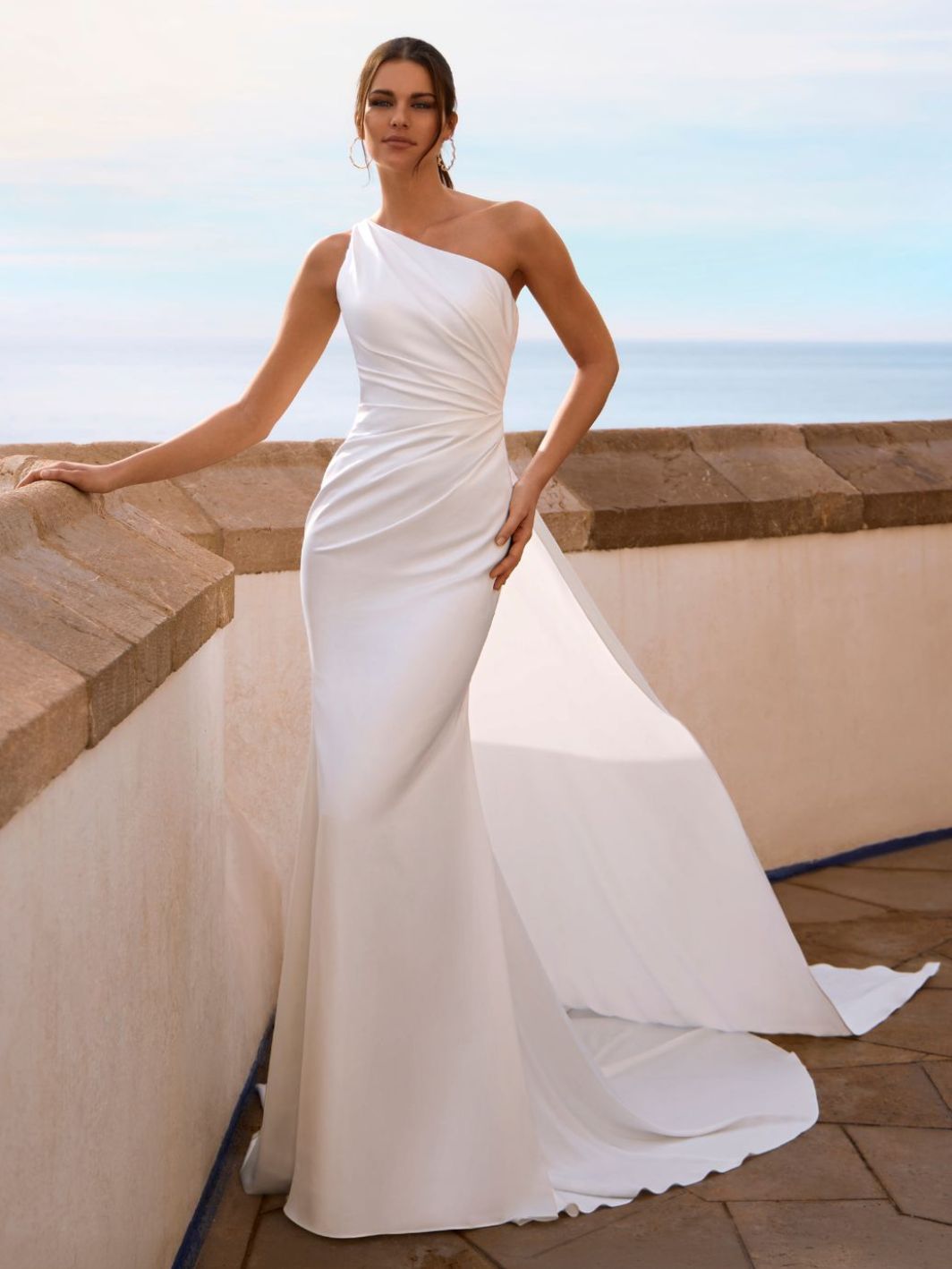 Schlichtes Fit-and-Flare-Brautkleid aus mattem Satin in Ivory, mit One-Shoulder-Ausschnitt, asymmetrischer Draperie und langer Schleppe. Angebot im Brautmodengeschäft Cuxhaven für Kundinnen aus Oldenburg und Bremen