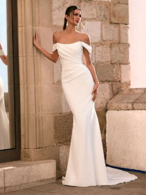 Schlichtes, figurbetontes Fit-and-Flare-Brautkleid aus mattem Satin in Ivory, mit drapiertem Korsagen-Oberteil und tief sitzenden Carmen-Trägern. Brautmode in Cuxhaven für Kundinnen aus Hamburg, Stade und Bremen.