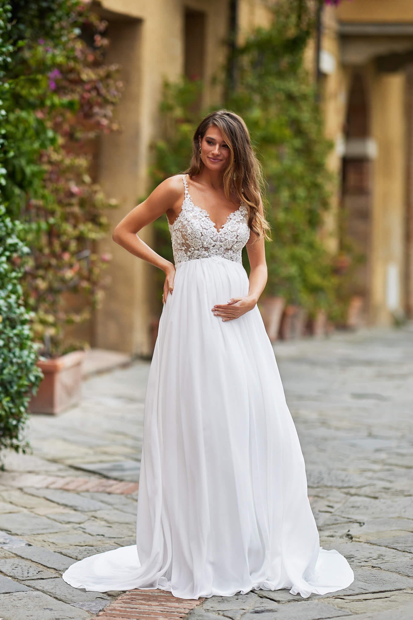 Umstandsbrautkleid im romantischen Empire-Stil mit filigranen Spaghettiträgern, glitzerndem Spitzenmieder und fließendem Chiffonrock, exklusiv erhältlich in Cuxhaven.